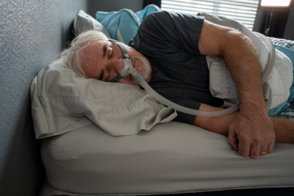 A man sleeps in a bed wearing a CPAP breathing machine